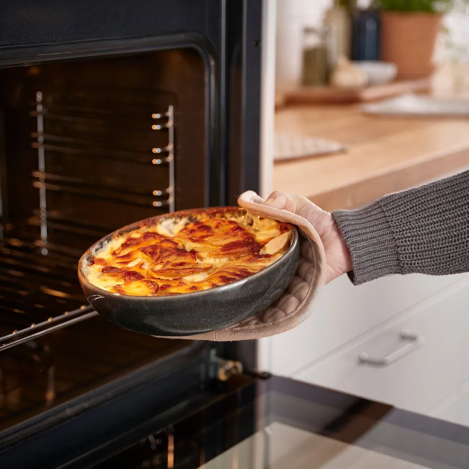 Person removing baked dish from oven, using a dark grey glazed plate.