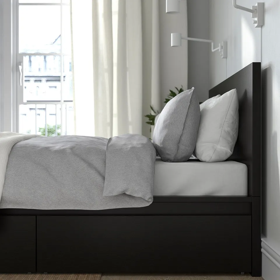 Bedroom scene with MALM bed, featuring grey bedding, pillows, and plant; wall light beside bed.
