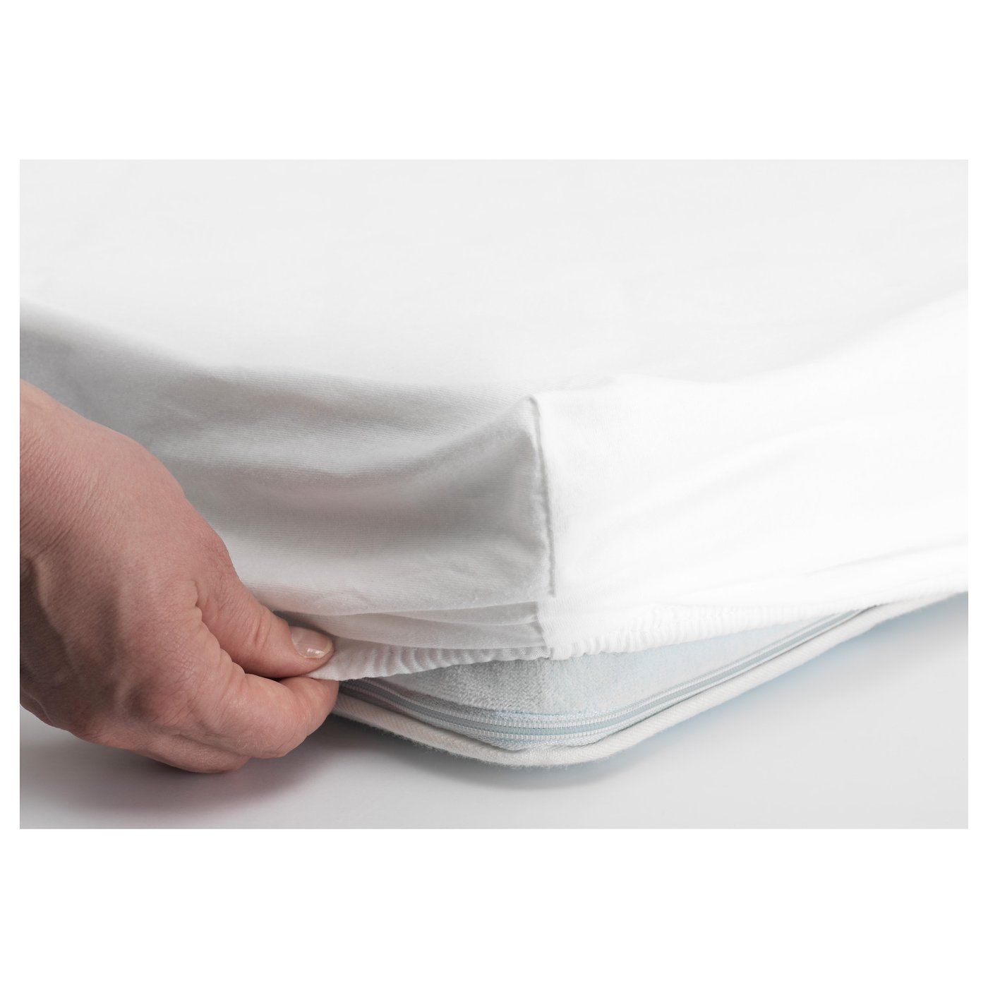 Hand pulling fitted sheet over mattress, demonstrating elastic edge for secure fit.
