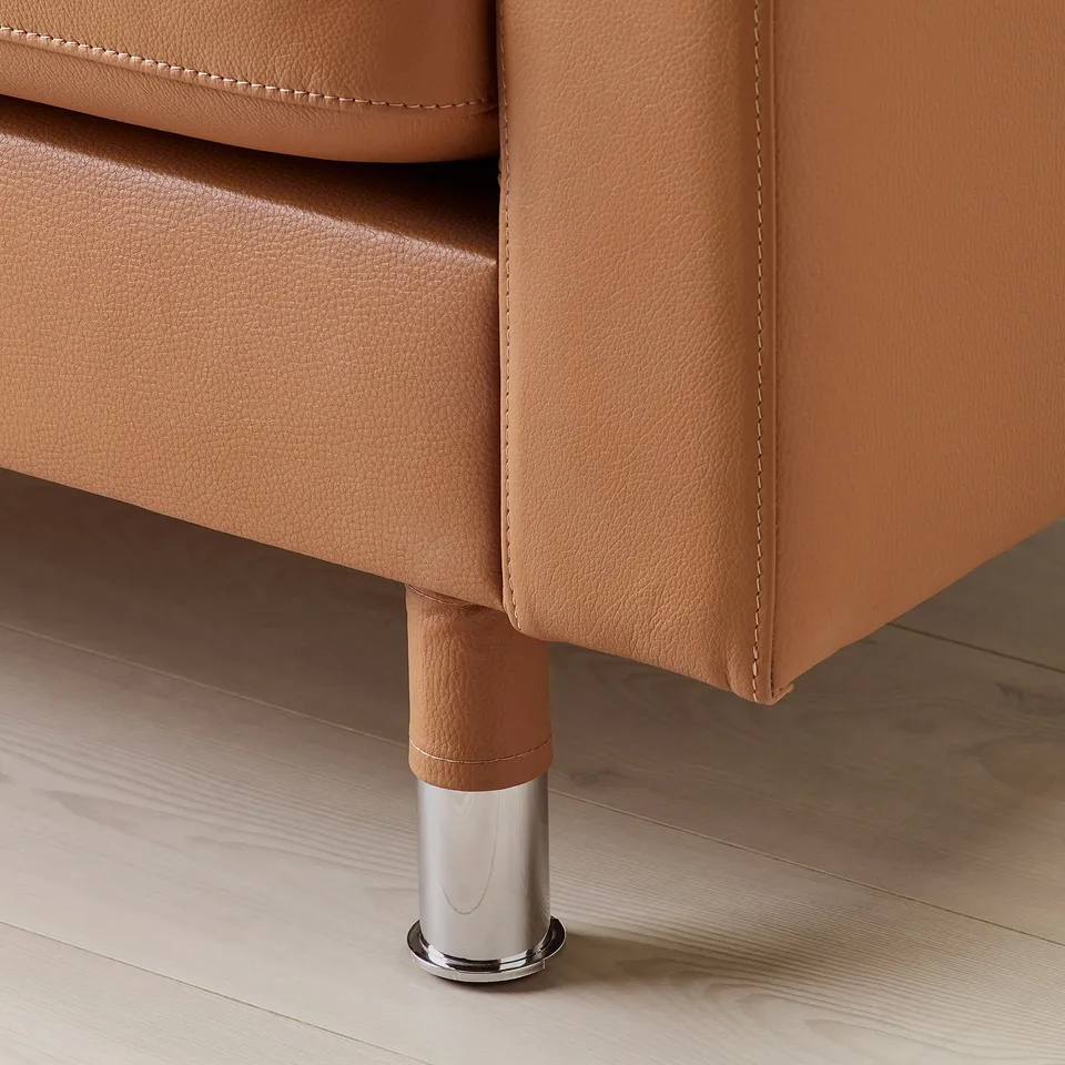 Close-up of a leather sofa with metal legs. Tan leather finish, visible stitching, and polished chrome leg detail.