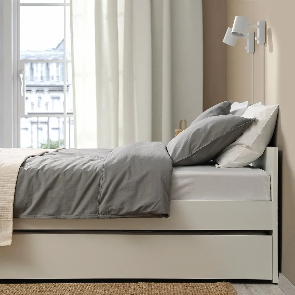 Daybed with trundle, storage, slatted base, grey bedding by window.