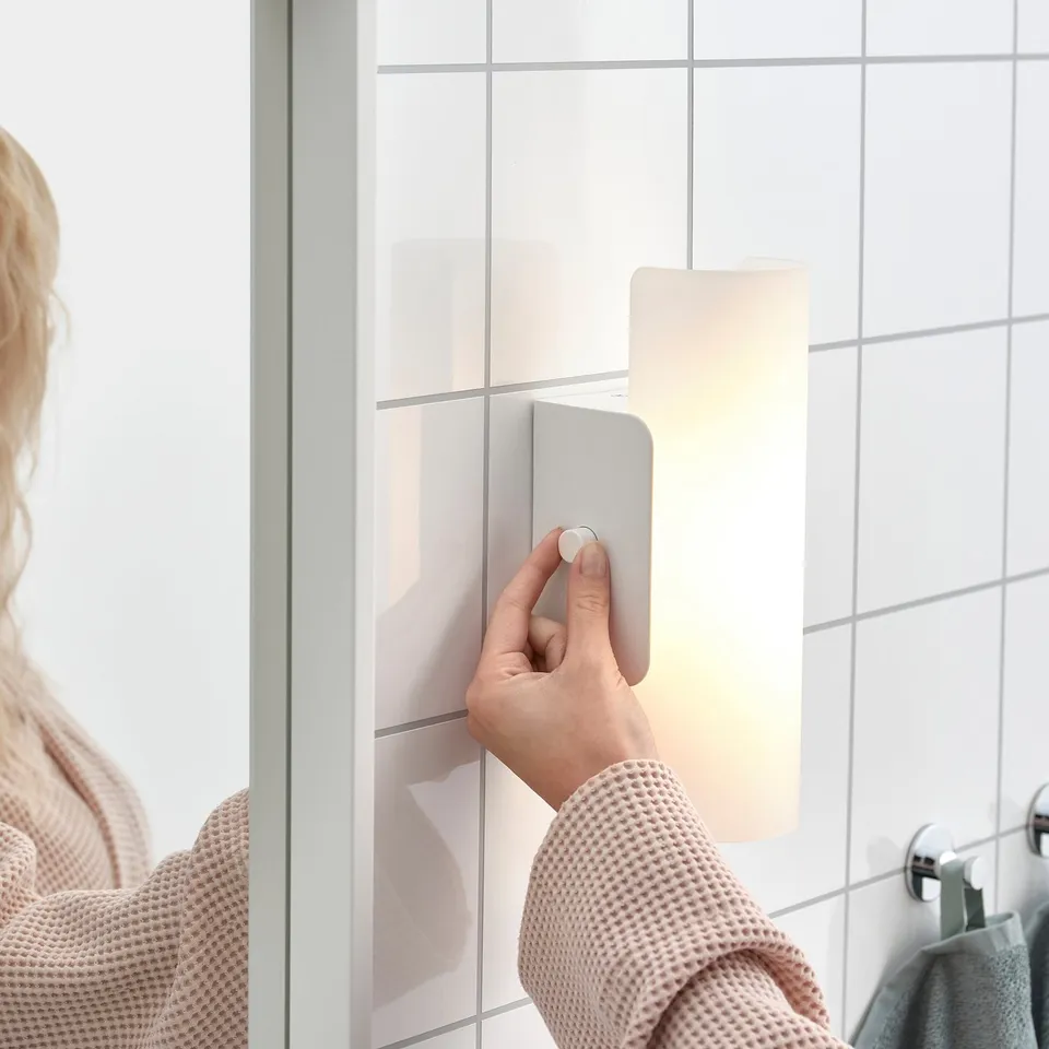 A person adjusts a dimmable, frosted glass bathroom wall lamp, saving energy and setting mood.