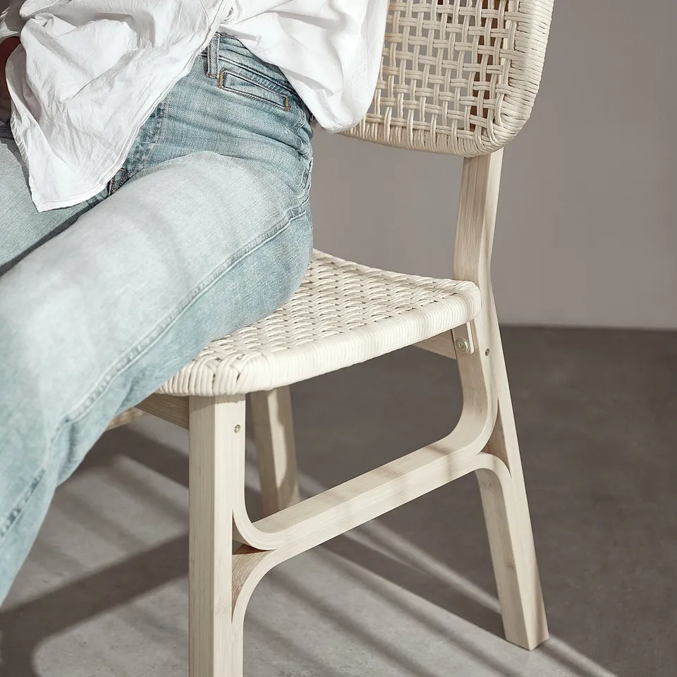 Person sitting on a light-colored wicker chair wearing a white shirt.