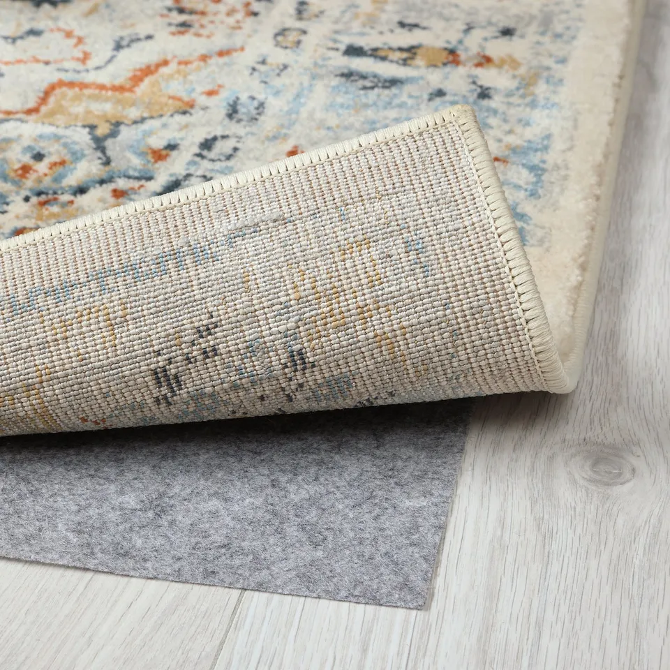 Decorative rug with intricate patterns, rolled back to show backing, placed on wooden floor.