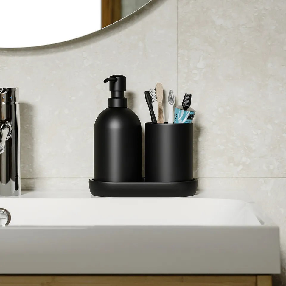 Black soap dispenser and toothbrush holder on white sink, part of GANSJÖN series. Dispenser has matte glass finish, tray included.