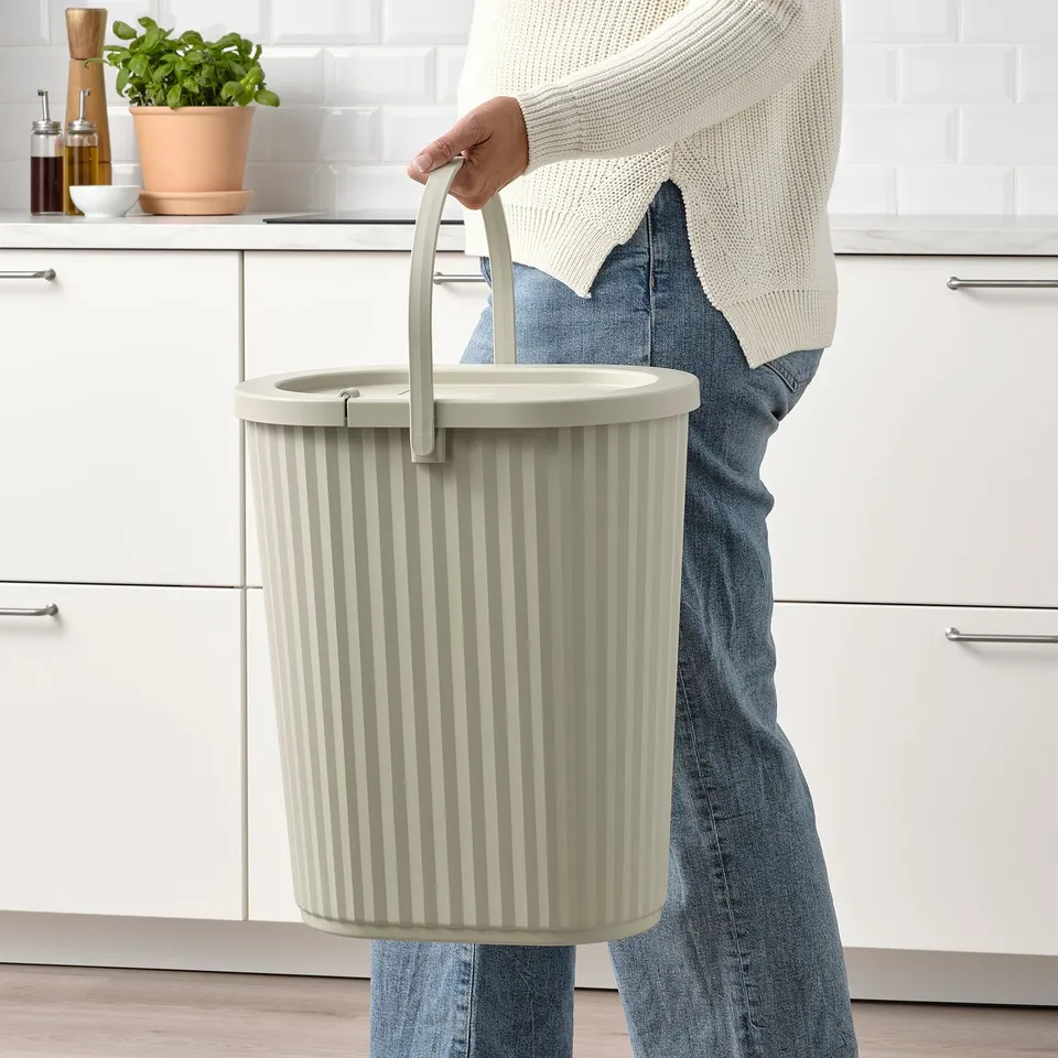 A person holding a white DAMMÄNG bin with a foldable handle, designed for indoor waste sorting and recycling.