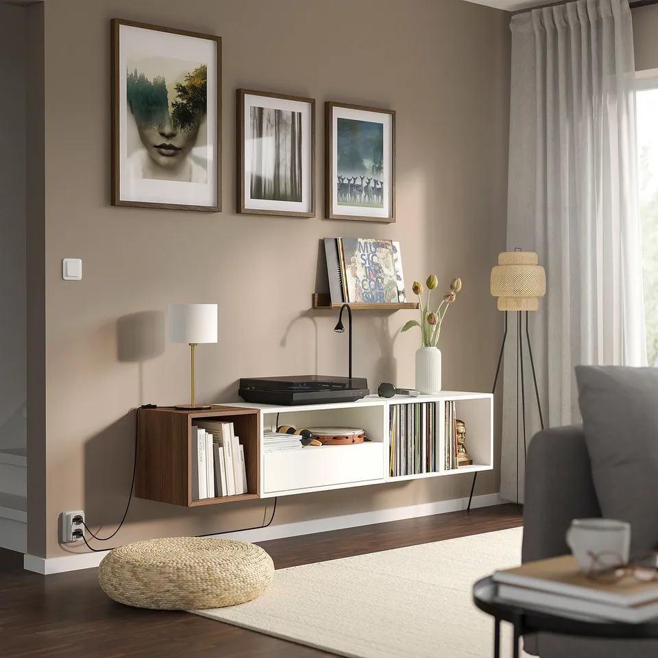 Modern living room with EKET shelves, books, records, and a lamp. Grey armchair, beige rug, and natural-contemporary style.