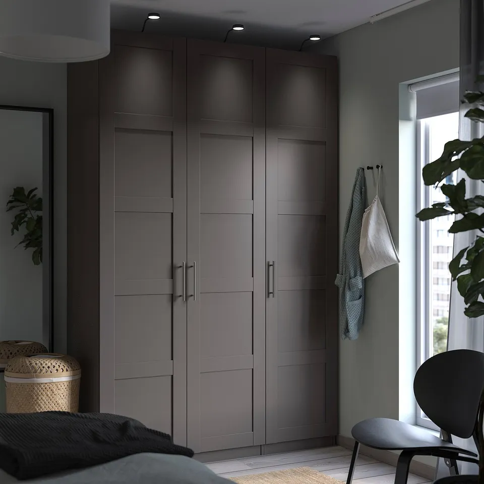Modern bedroom with grey PAX wardrobe, white chair, and green plants near window.