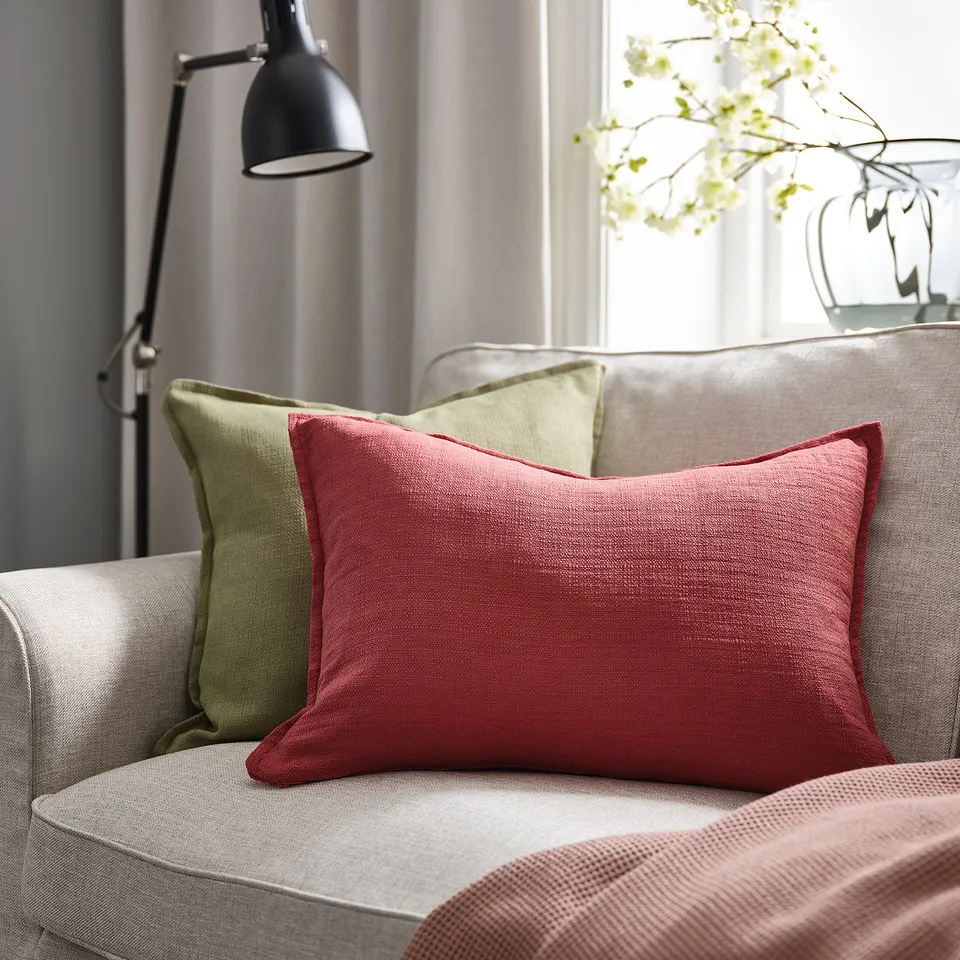 Red rectangular LAGERPOPPEL cushion on grey couch, with green pillow, modern design, small size.