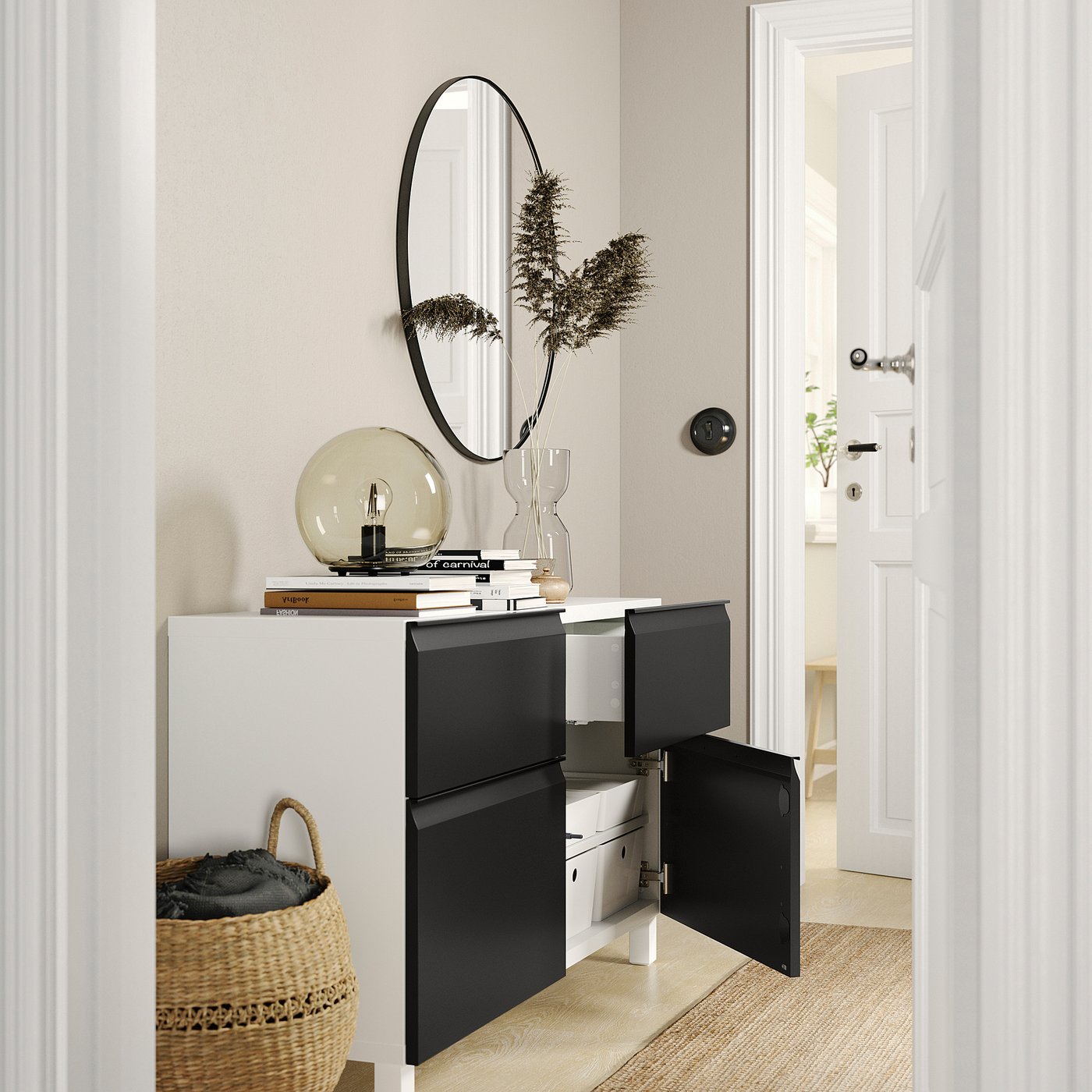 Modern entrance with white and black BESTÅ sideboard, round mirror, plant, lamp, books, and basket.