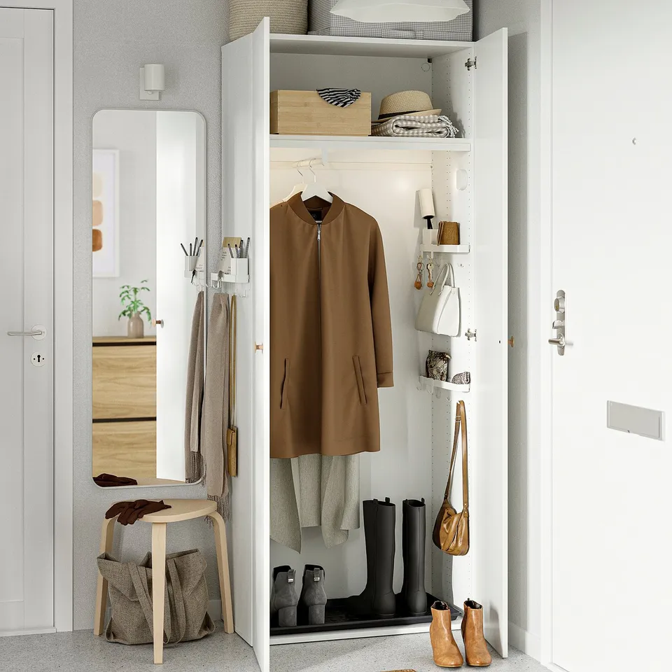 A white wardrobe organiser with hooks, shelves, and a container. It stores coats, boots, and bags, utilising wall space efficiently.