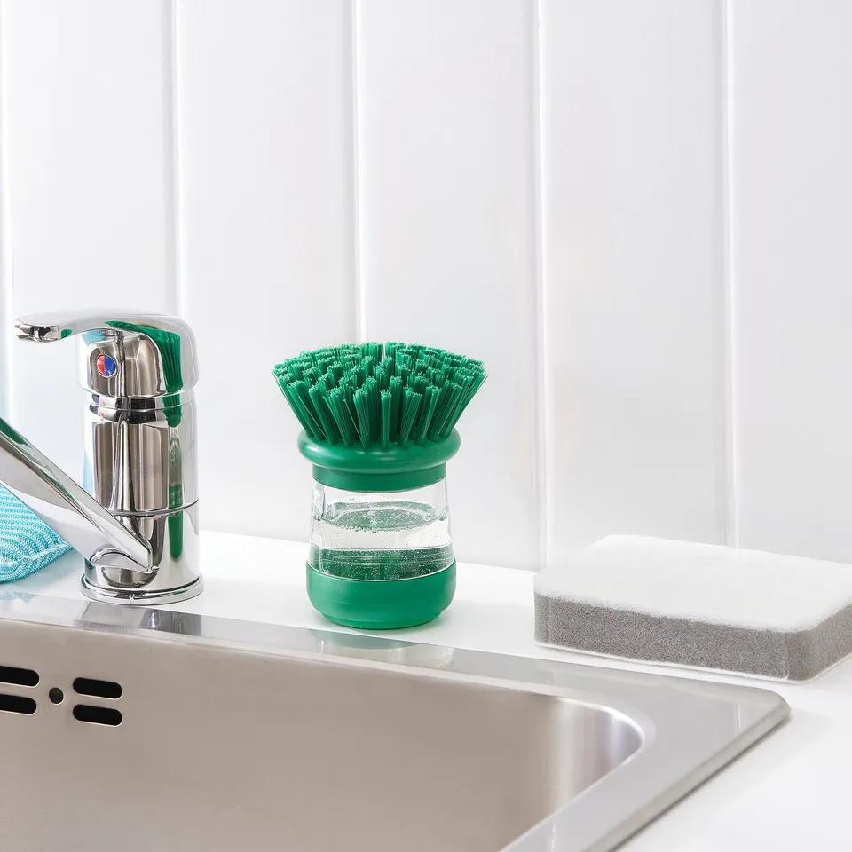 Kitchen sink with green dish brush, soap dispenser, and sponge.