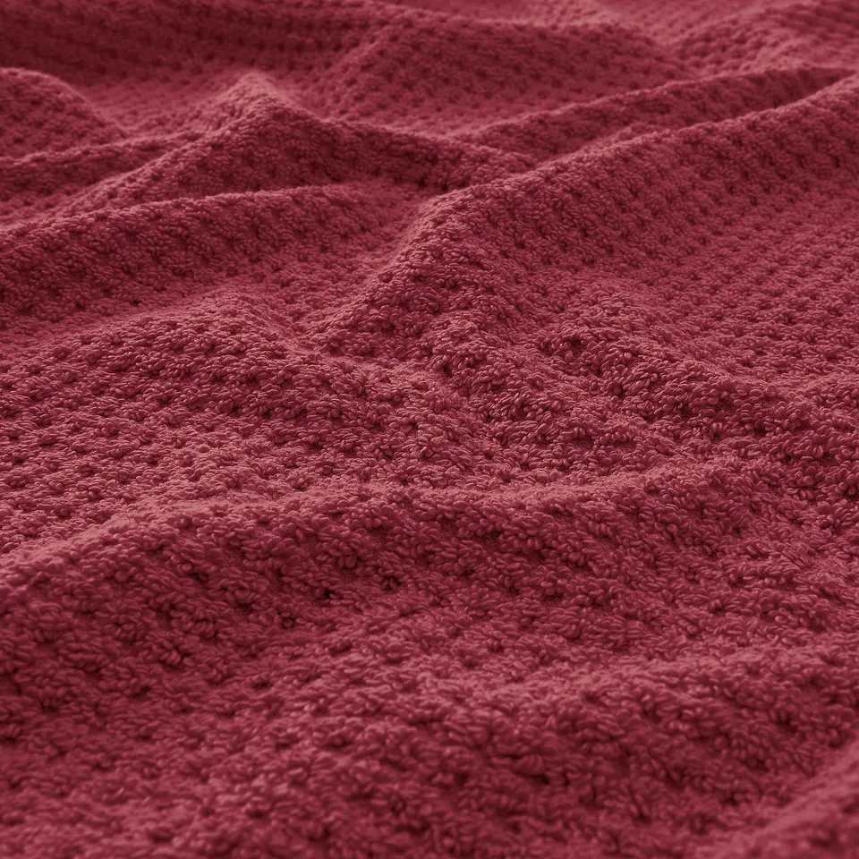 Close-up of soft, textured, red cotton towel showcasing its fluffy, absorbant quality.