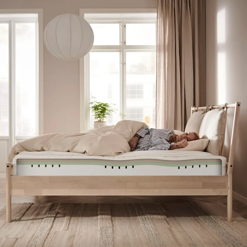Person sleeping peacefully on a white ÅKREHAMN foam mattress in a modern beige room.