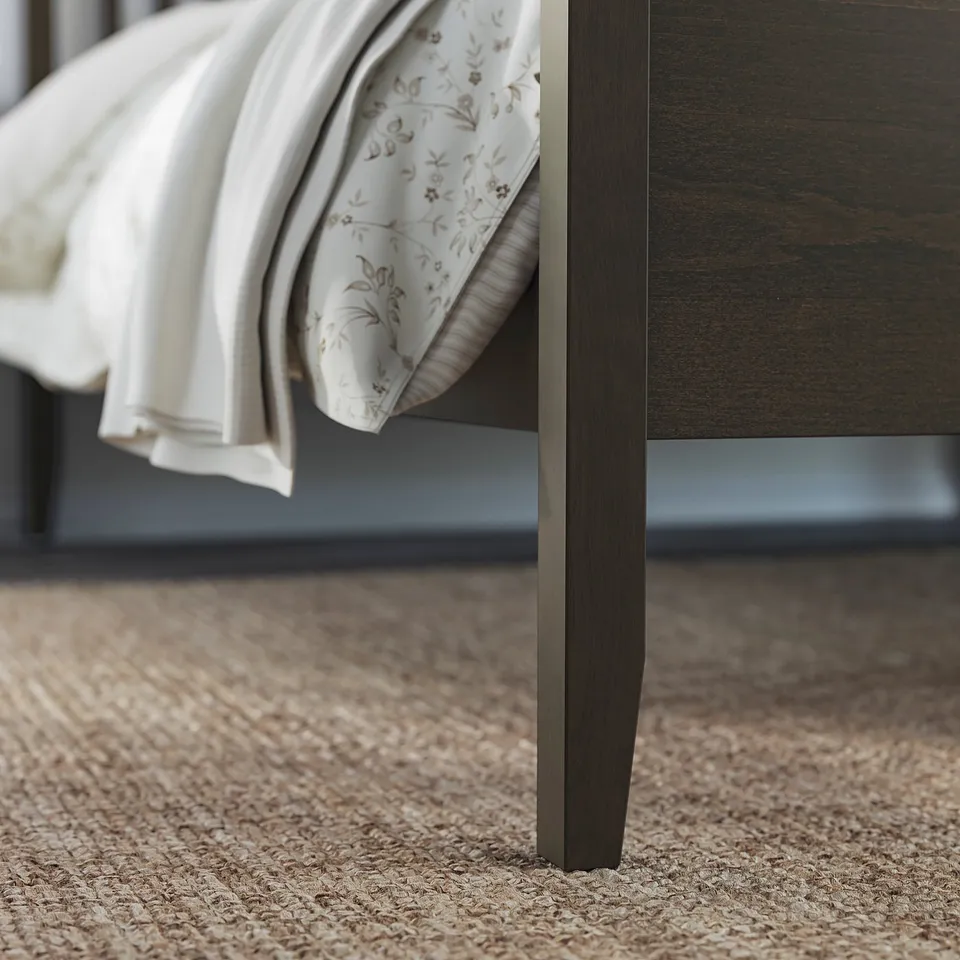 Wooden bed frame with dark finish, white blanket with floral print neatly folded.