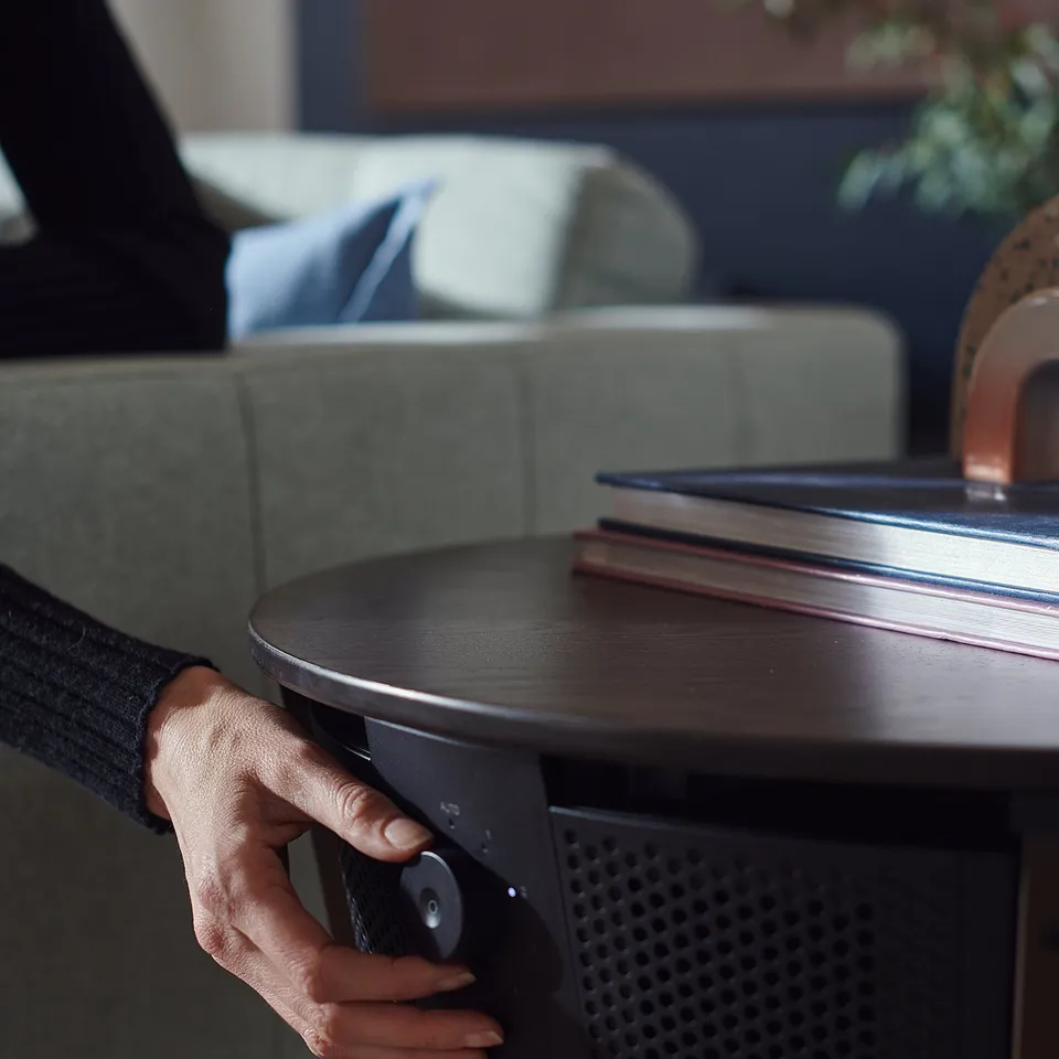 Image description: a hand adjusts a black ikea STARKVIND air purifier table in a cozy living room.