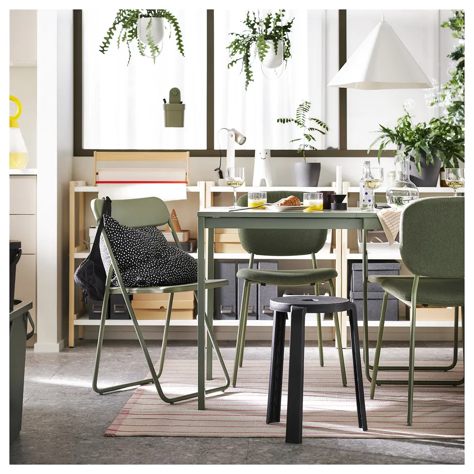 Bright dining room with off-white rug, green chairs, wooden table, white curtains, hanging plants, and pendant lights.