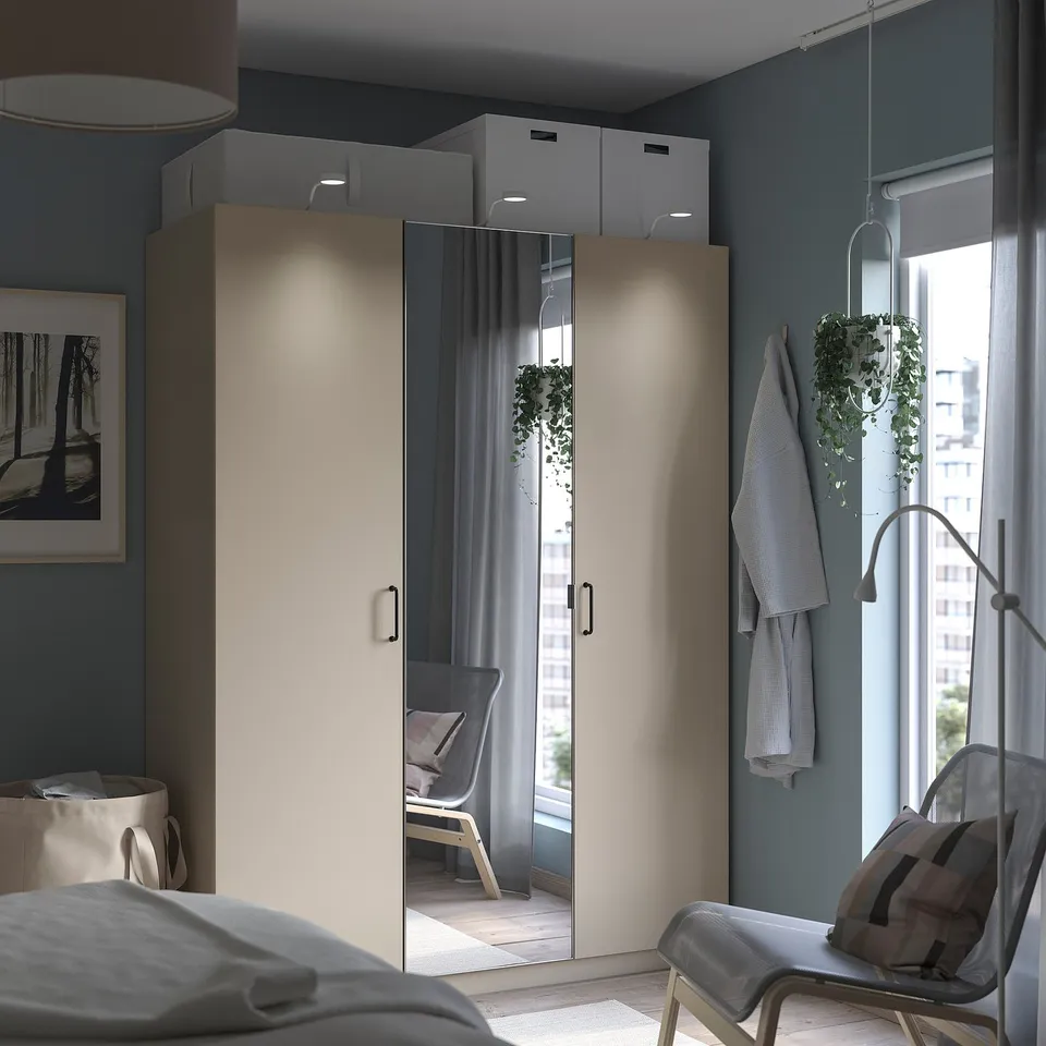 Modern bedroom with grey PAX wardrobe, mirrored doors, soft lighting, and hanging plants.