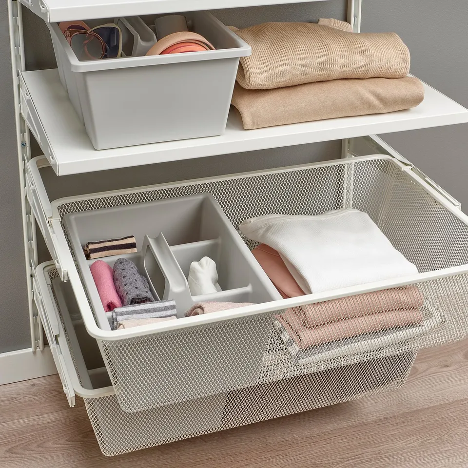 White mesh drawer organiser with four compartments for small items. Shelves above with bin and folded clothes.