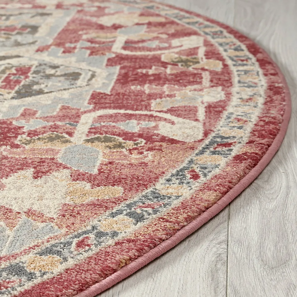 Round, ornate rug with warm colours on a light wooden floor. Detailed, traditional patterns with a soft, modern look.
