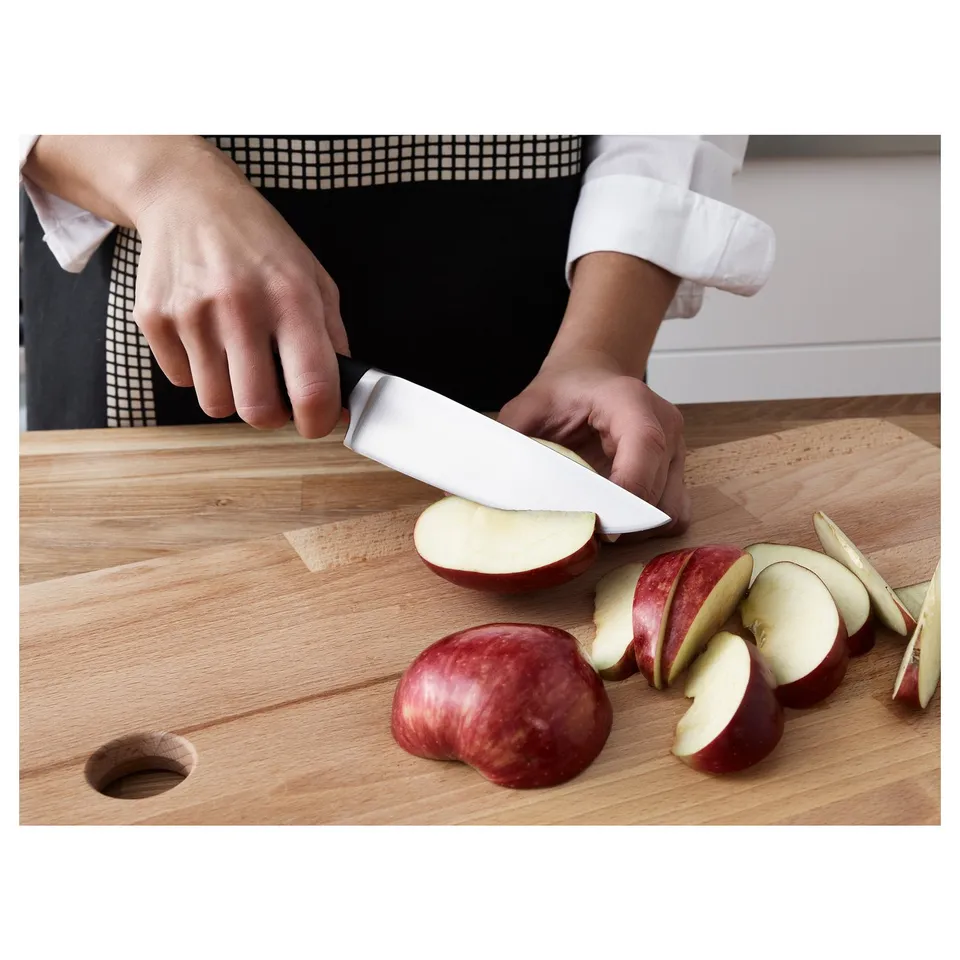 Person slicing apple on wooden cutting board with sharp knife.