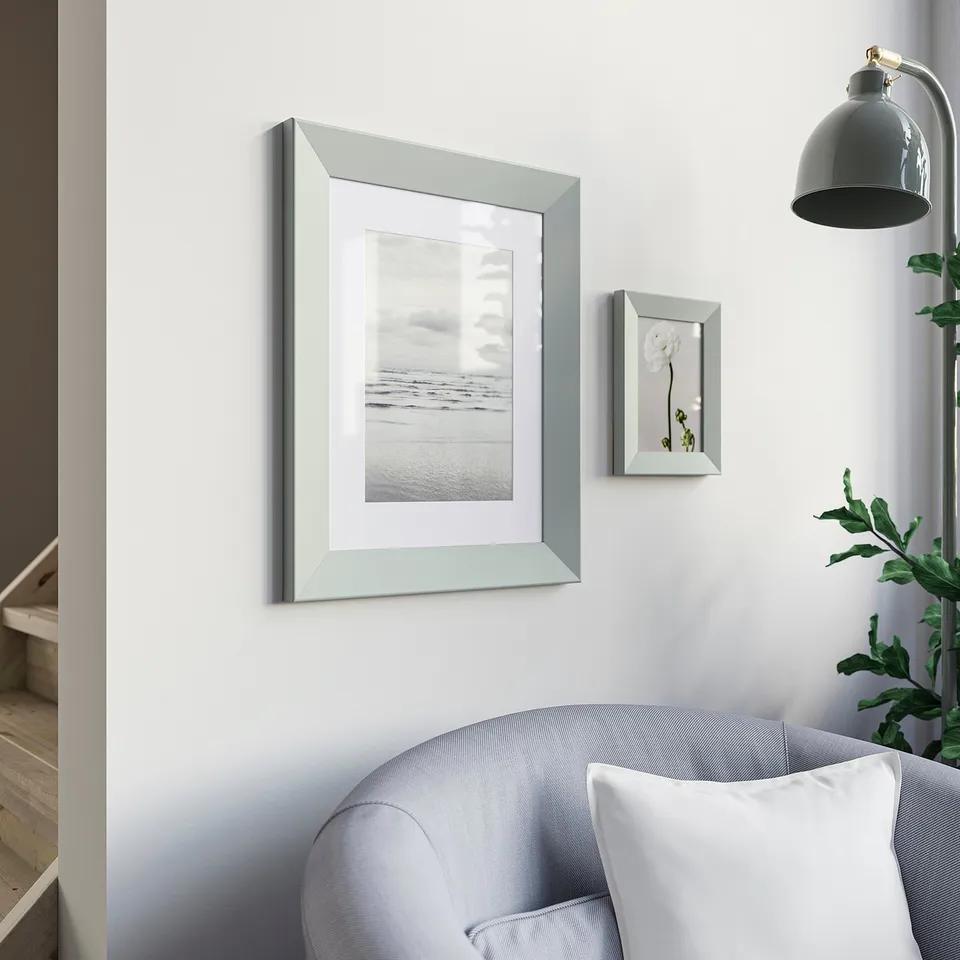 Two silver frames: beach & floral. Blue chair, gold lamp, greenery.