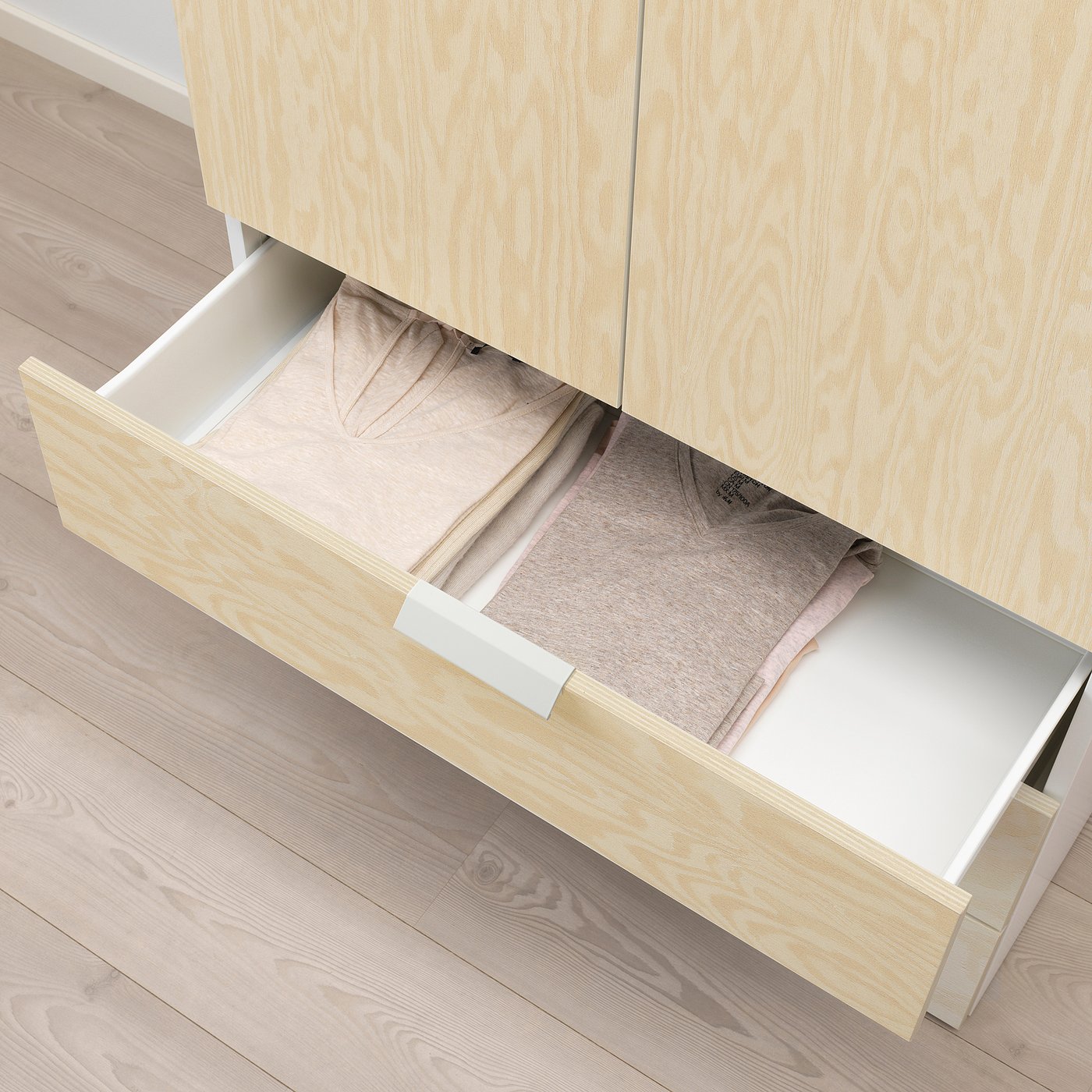Wooden drawer open, revealing neatly folded clothes inside. Part of a storage system with light-colored frames.
