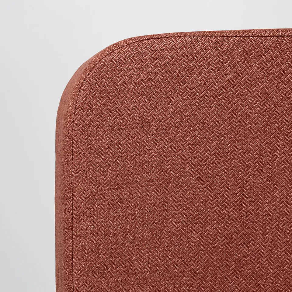 A close-up of a red upholstered sofa corner, showing high-quality fabric with a neat stitching line.