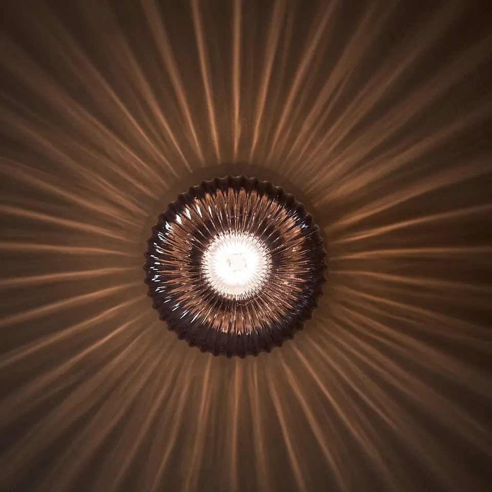 Round brass lamp with clear glass, emitting soft golden light, mounted on ceiling.