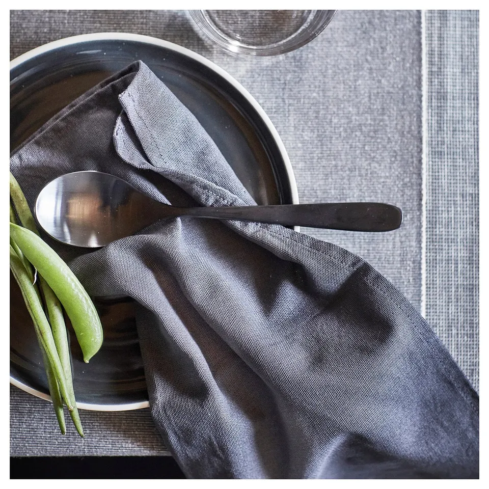 SVARTSENAP grey cotton table runner; rectangular, simple design with neatly folded edges; includes green beans, spoon, and dark napkin on top.