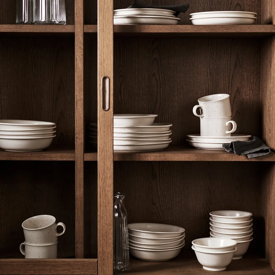 Wooden shelves with light beige DAGGASTER stoneware dishes, including bowls, mugs, and plates in earthy tones, neatly organised.