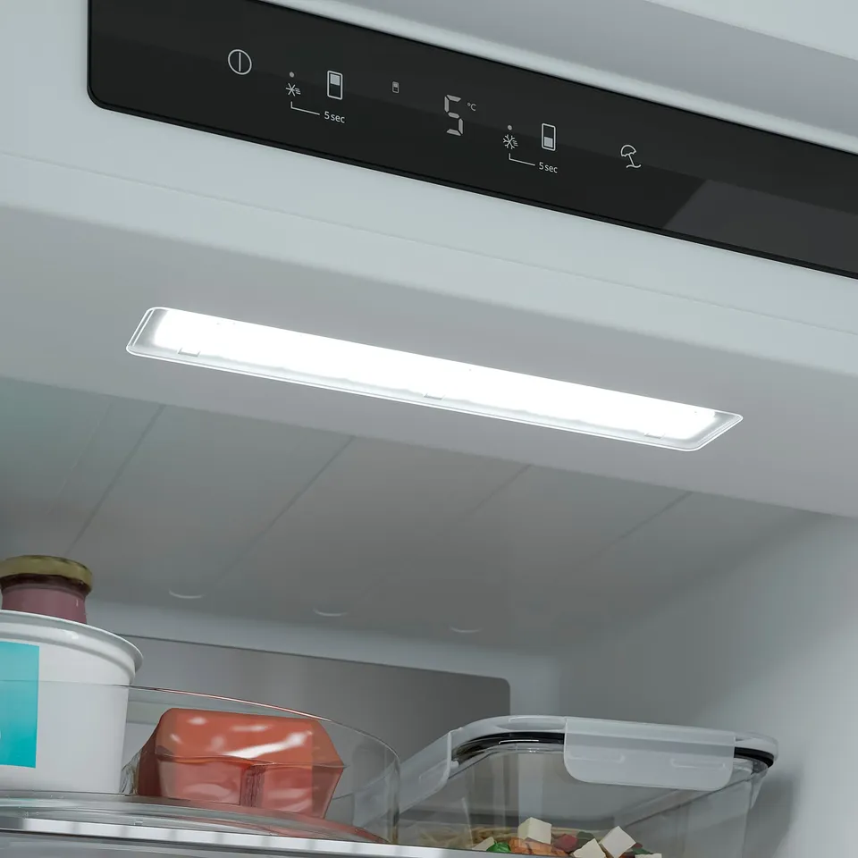 Image shows a fridges interior with led light on, illuminating food containers; control panel visible above.