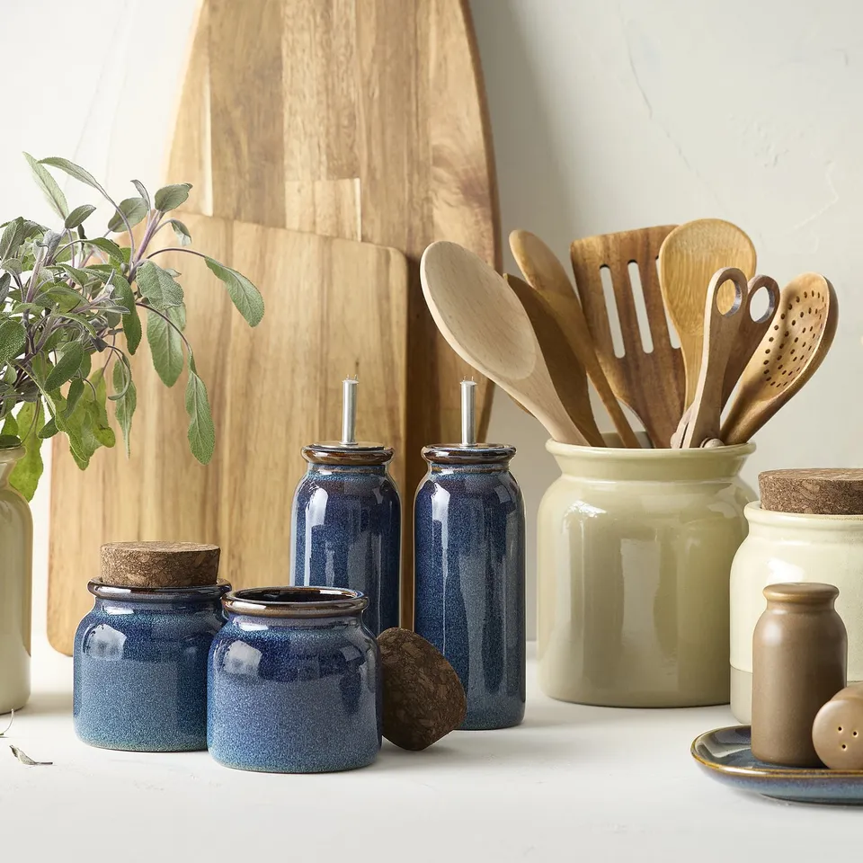 BRUGDHAJ blue jars and olive jar display, wooden utensils, plant, and cutting board. Jars are medium-sized compared to utensils.