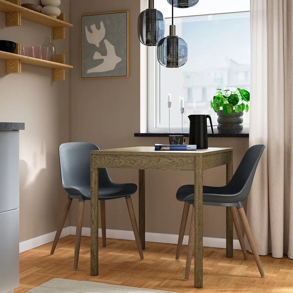 Small dining area with GRÖNSTA chairs in grey; wooden table, art, plants, and modern decor.