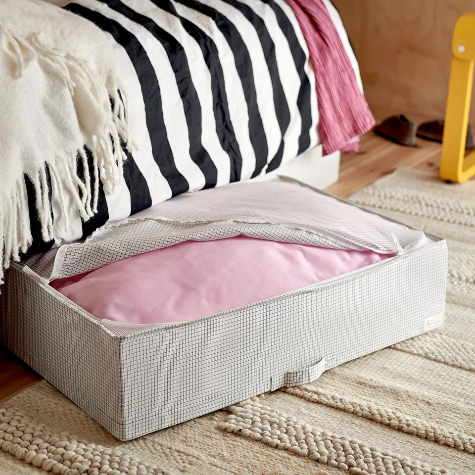 Open storage box under couch, contains pink blanket, beige colour with handles.