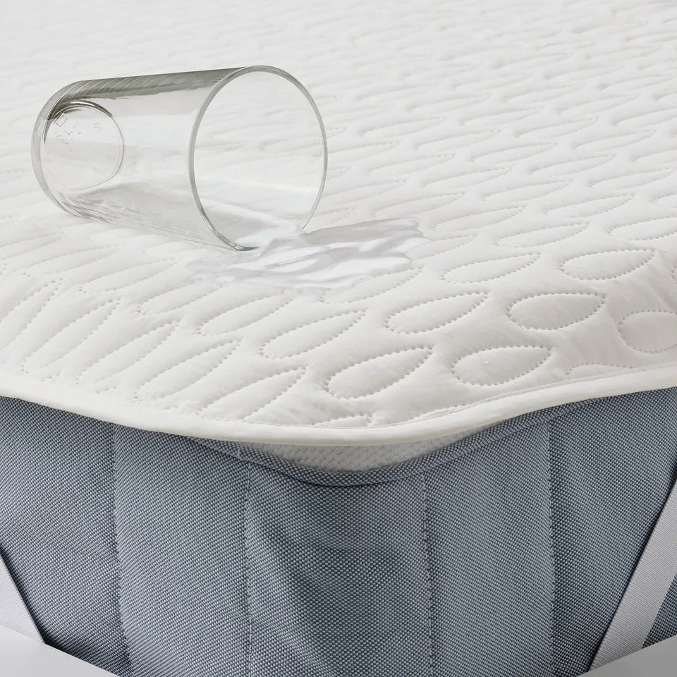 A transparent glass tipped over on a white mattress protector, demonstrating its waterproof functionality.