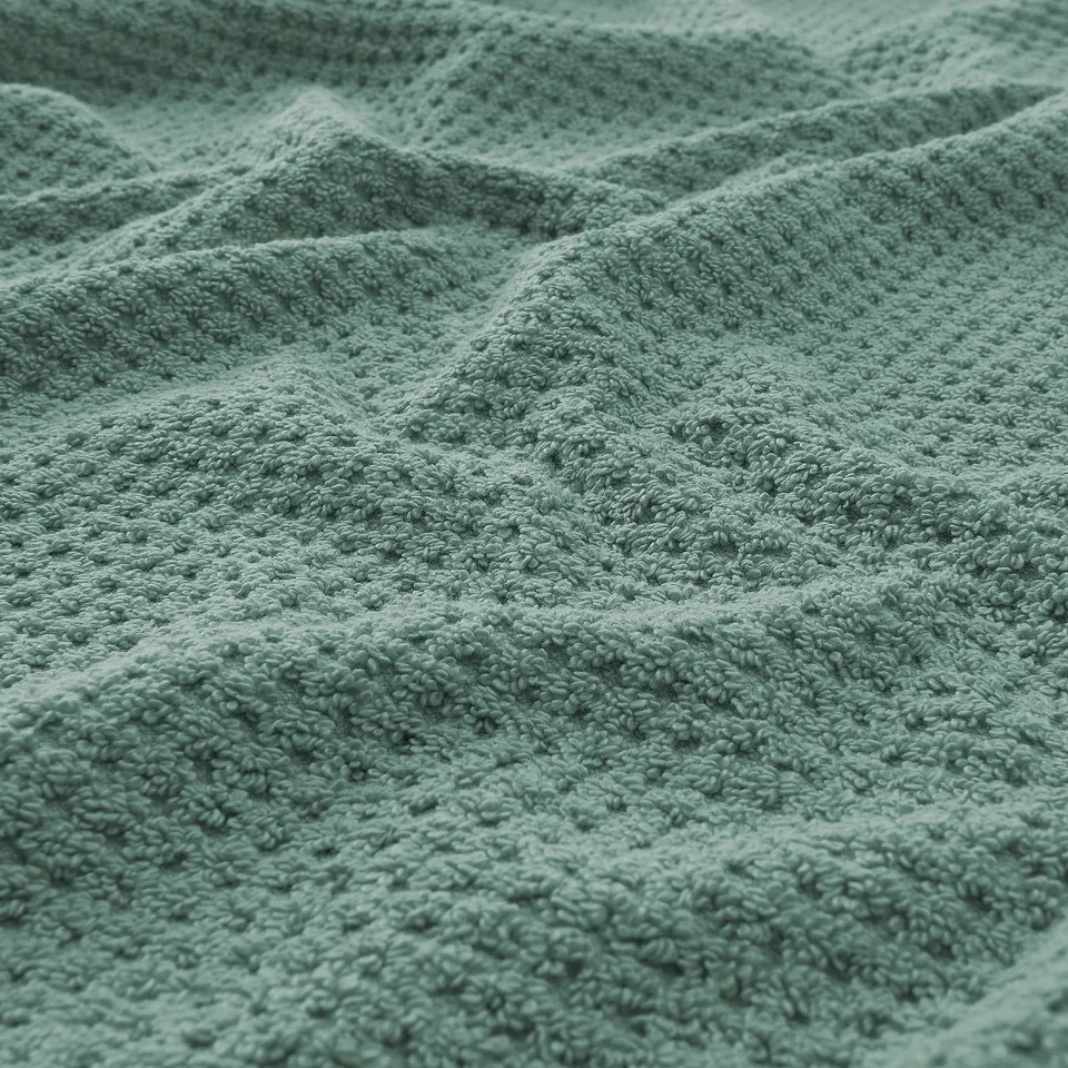 Close-up of luxuriously soft, textured green towel showcasing its plush, absorbent fibres.