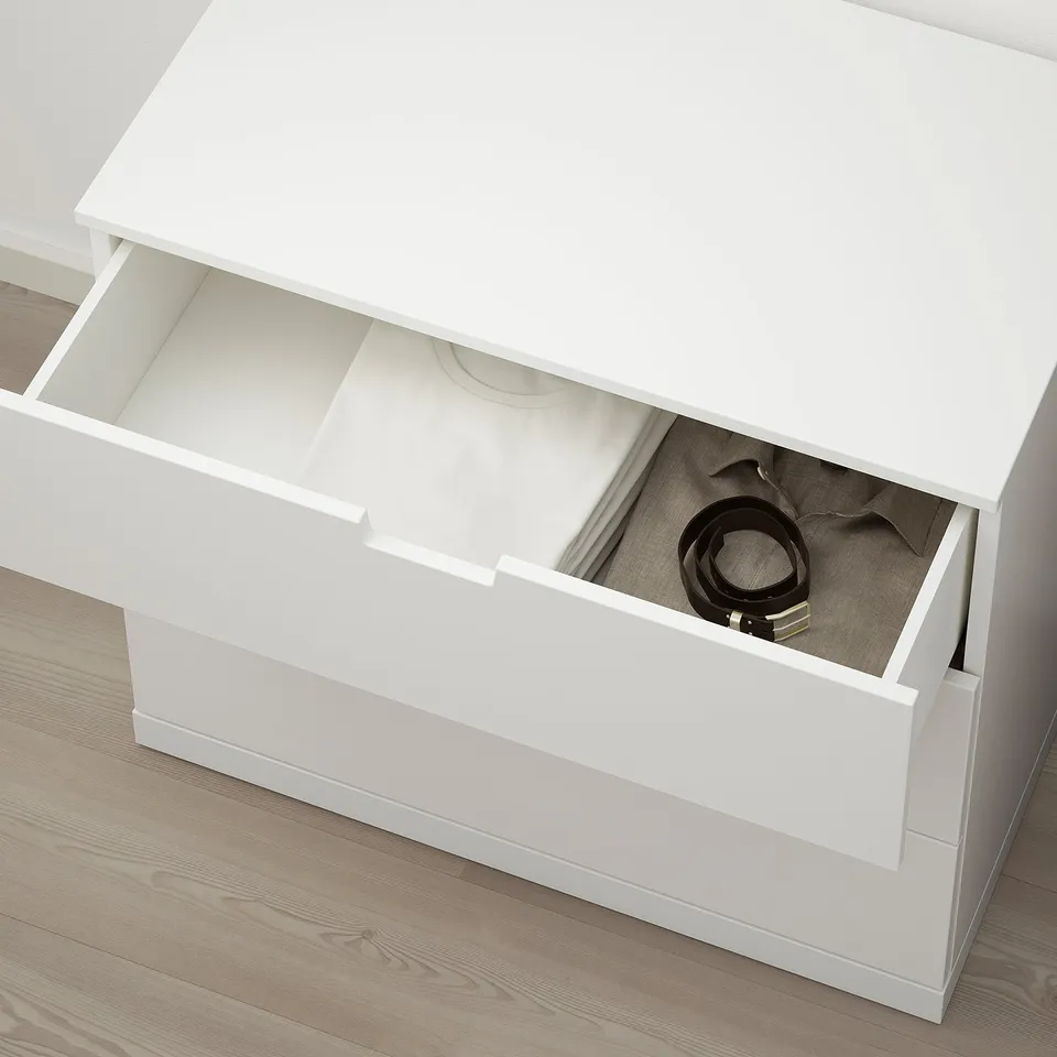 A white NORDLI chest of drawers with one open drawer revealing a belt and other items inside.