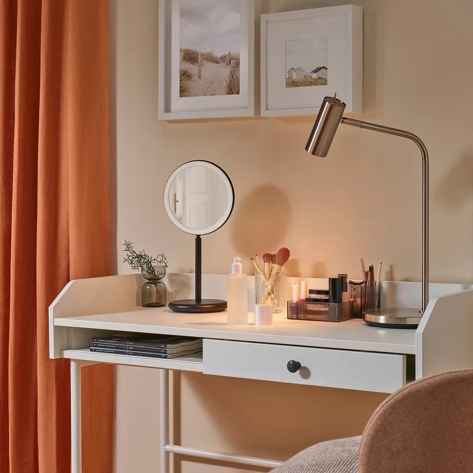 A modern vanity desk with a lit magnifying mirror, makeup, and decor.