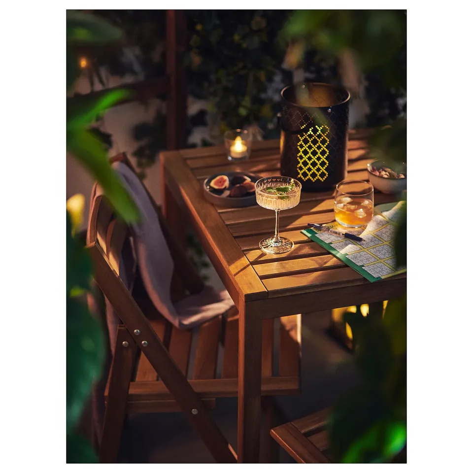 Wooden NÄMMARÖ table set outdoors with drinks, snacks, and cosy blankets.