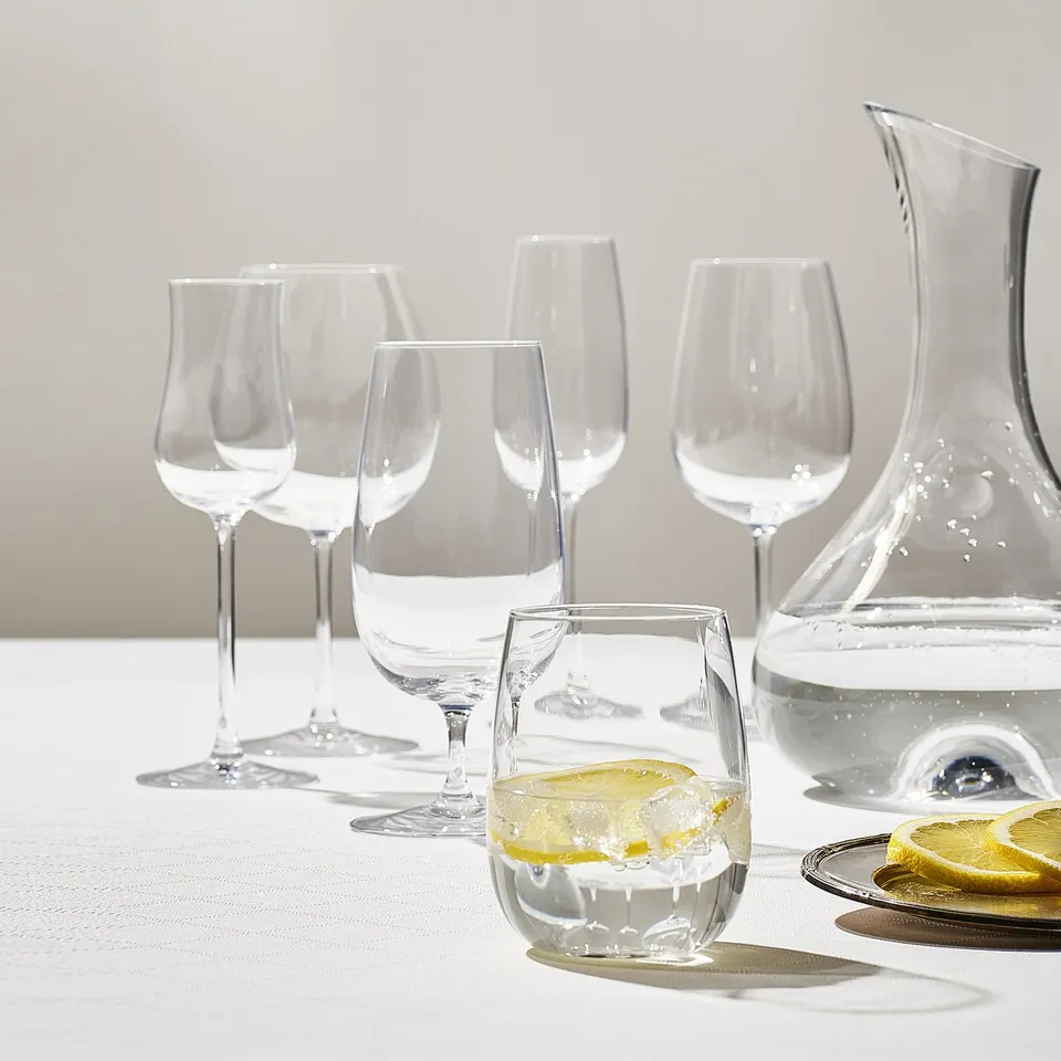 Six clear STORSINT glasses vary in size and shape, one with lemon. Crystalline, elegant, perfectly arranged on a white table.