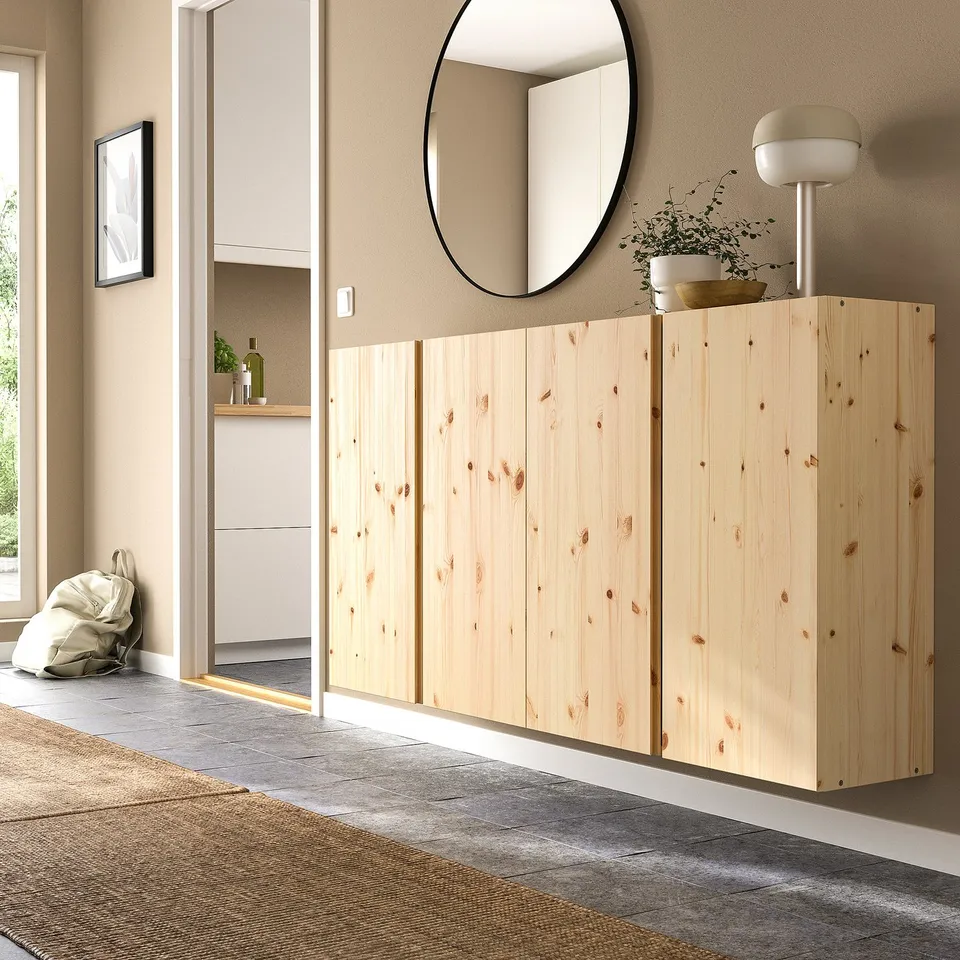 Wooden IVAR cabinets, mirror, lamp, and plant in modern room. Pine storage fits corner next to closet. Complements grey floor and beige walls.