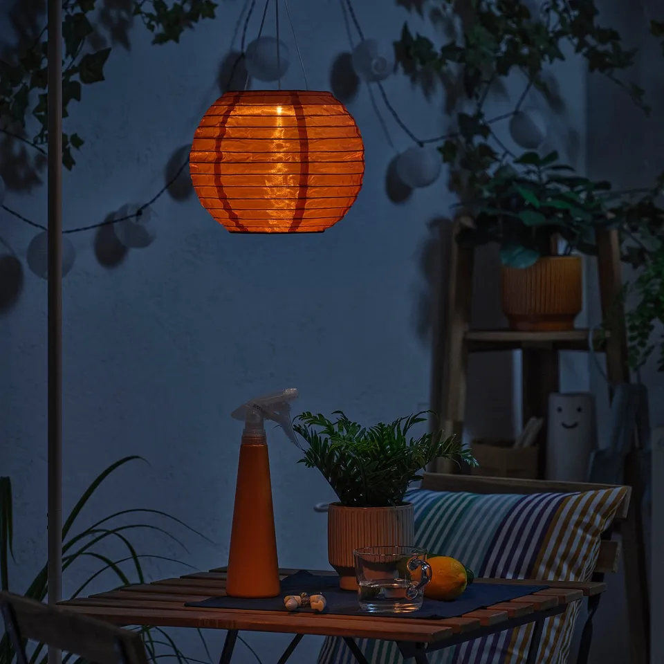 Small outdoor table set with an orange lantern, plant, glass, and lemon. The lantern illuminates the area, creating a cosy atmosphere.