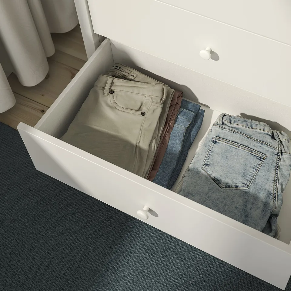 Open white drawer showing folded pants and jeans, demonstrating organised storage.
