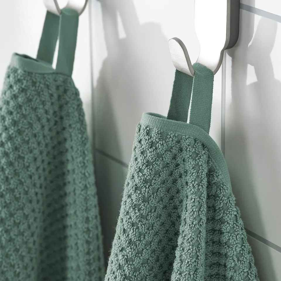 Two green cotton towels hang neatly on hooks, showcasing their soft, fluffy texture and absorbent qualities.