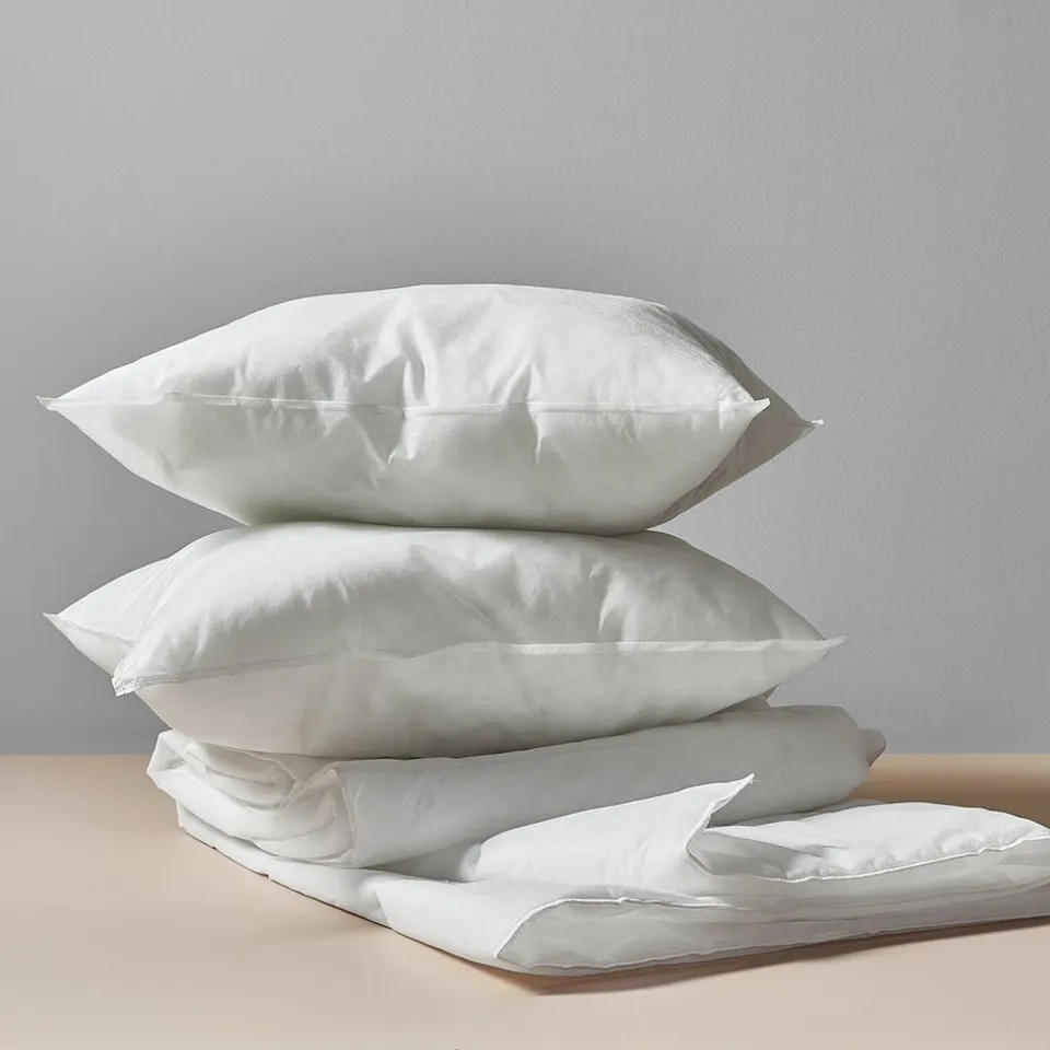 Stack of four white pillows on a table against a wall.