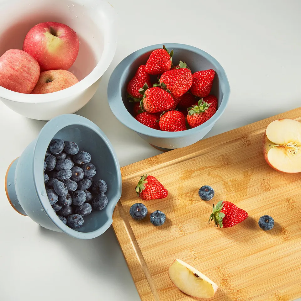 Three bowls of fruit on a cutting board. Left: blueberries, middle: strawberries, right: apples. A PONNYFISK bowl with a spout and handle.