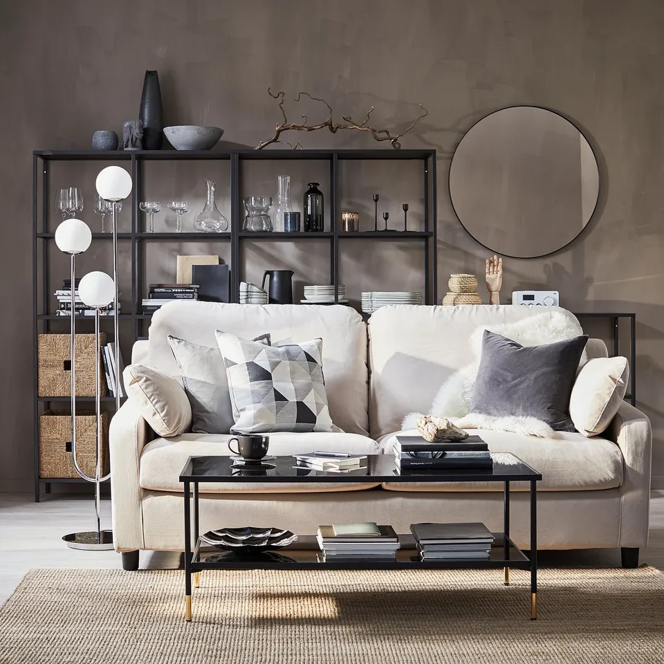 Modern living room with beige sofa, black coffee table, glass and chrome lamp, black and white decor, grey wall.