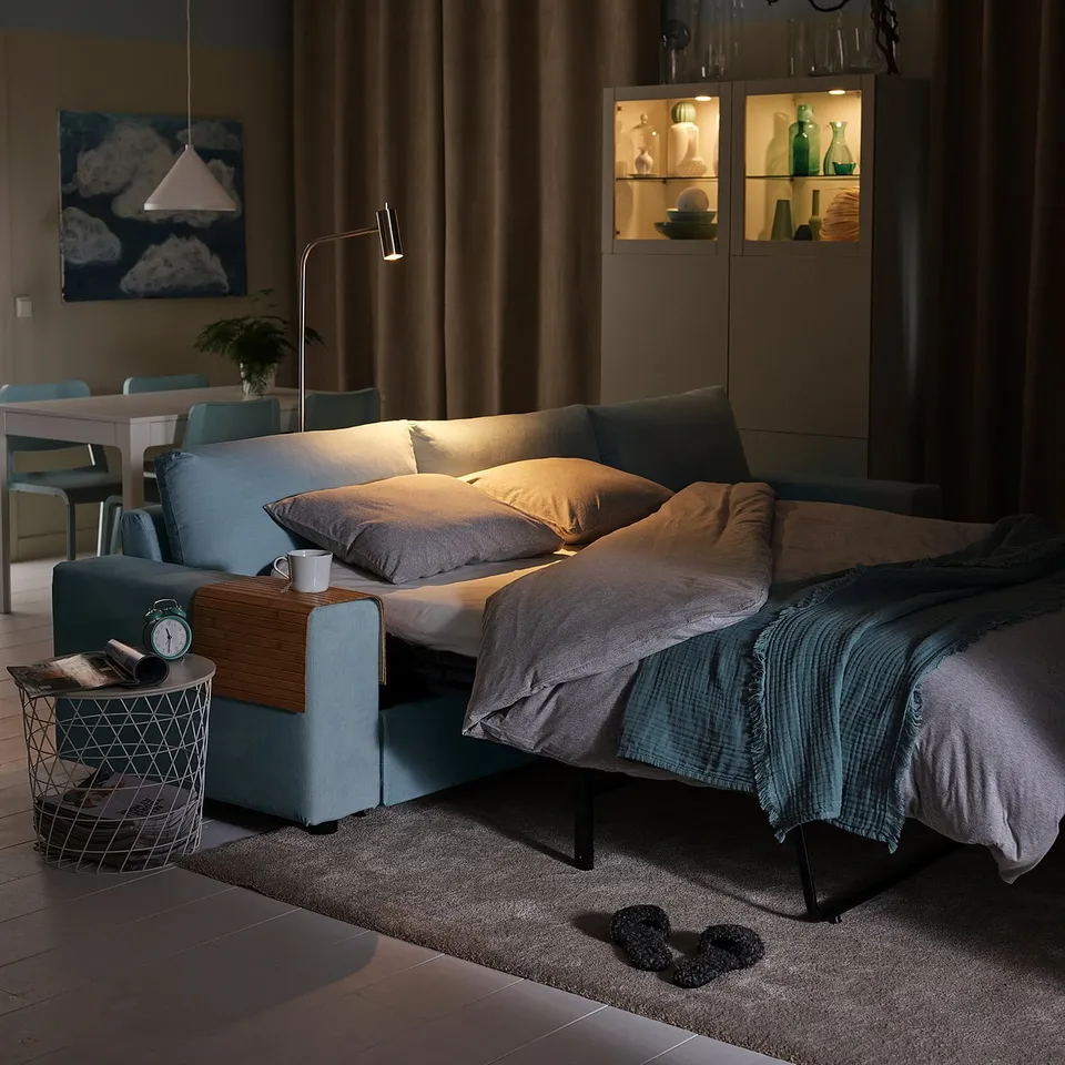 Modern dimly lit living room with blue sofa, wooden tray, grey curtains, and wall artwork.