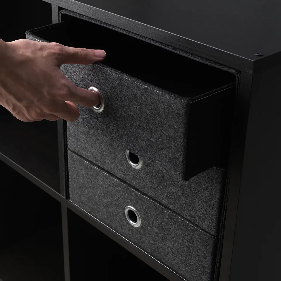 Person opening a dark grey fabric drawer with metal handles on black furniture.